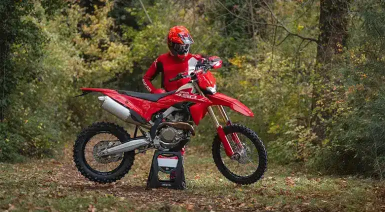 Ducati Desmo450 EDS Enduro-Motorrad in einer herbstlichen Waldumgebung mit Fahrer in roter Ausrüstung.