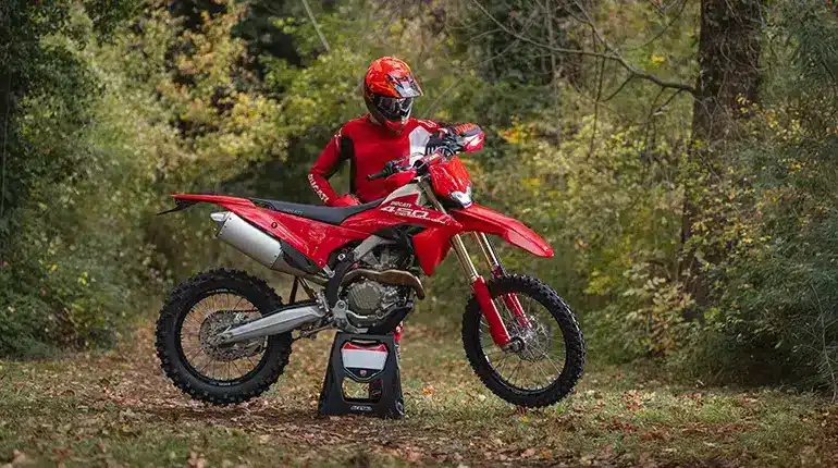 Ducati Desmo450 EDS Enduro-Motorrad in einer herbstlichen Waldumgebung mit Fahrer in roter Ausrüstung.