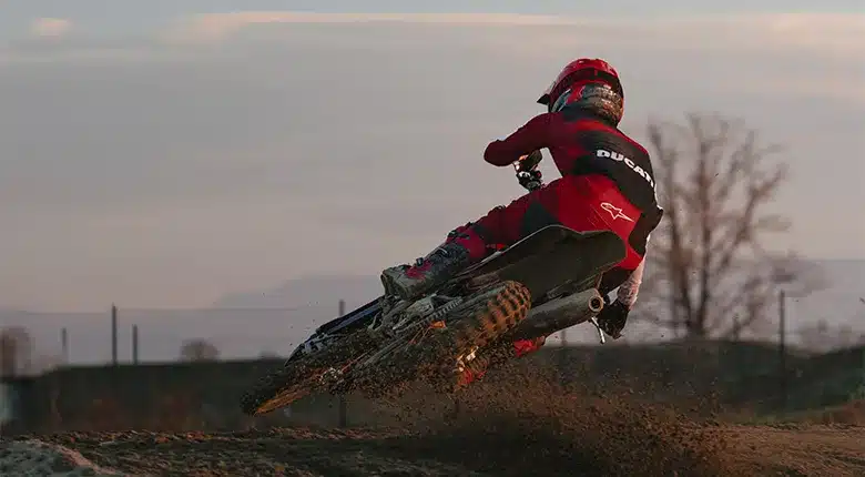 Fahrer auf Ducati Desmo450 MX Factory beim Kurvendrift auf Offroad-Strecke, bei Sonnenuntergang.
