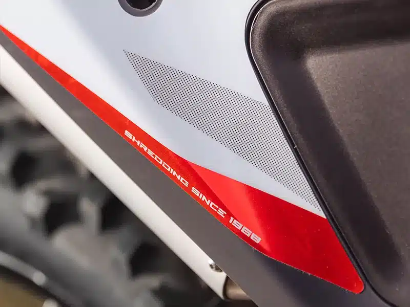 Nahaufnahme der Seitenverkleidung einer Fantic XE 125 2026 mit rotem Streifen und Aufschrift 'Shredding since 1968'.