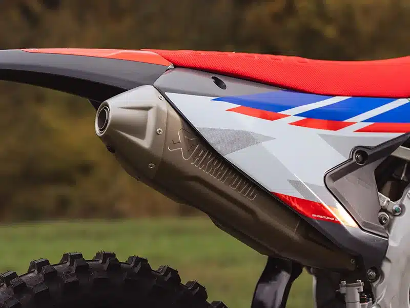 Nahaufnahme des Akrapovic-Endschalldämpfers an der Fantic XXF 450 MY26 mit roter Sitzbank und grafischen Designelementen.
