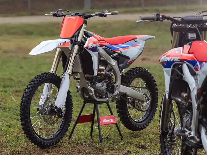 Fantic XXF 450 MY26 Viertakt-Motocross-Motorrad mit Kayaba-Fahrwerk und Akrapovic-Abgasanlage, abgestellt auf einer Wiese.