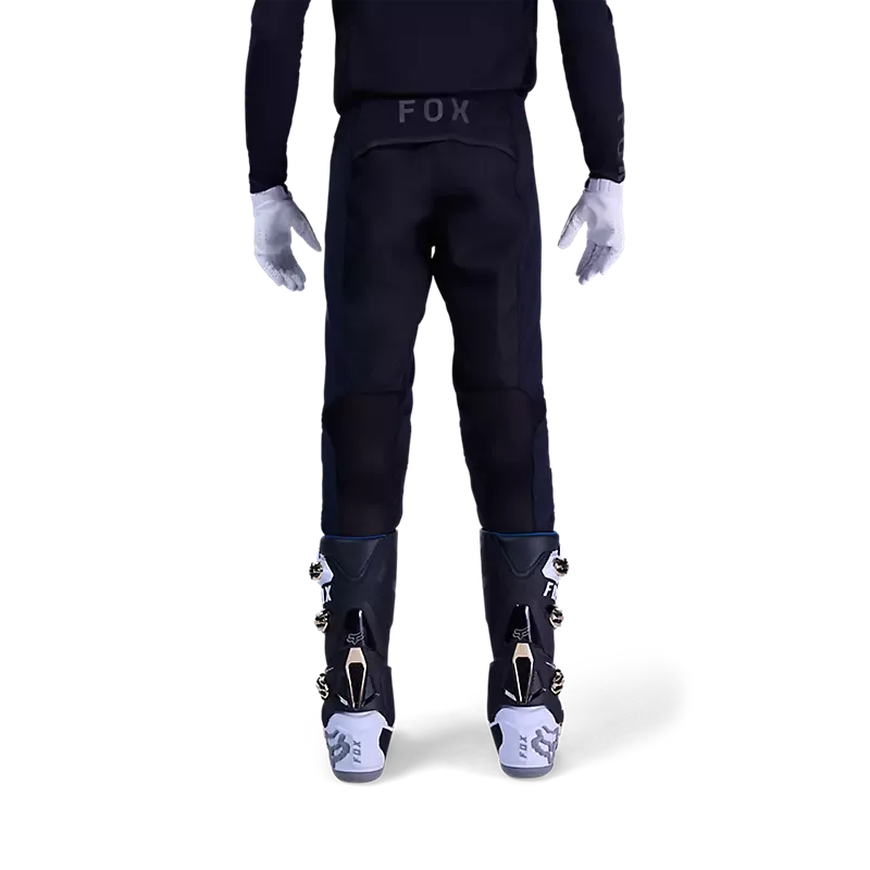 Das Bild zeigt die Rückansicht einer schwarzen Flexair Blackout Motorrad-Hose an einer stehenden Person mit Stiefeln.