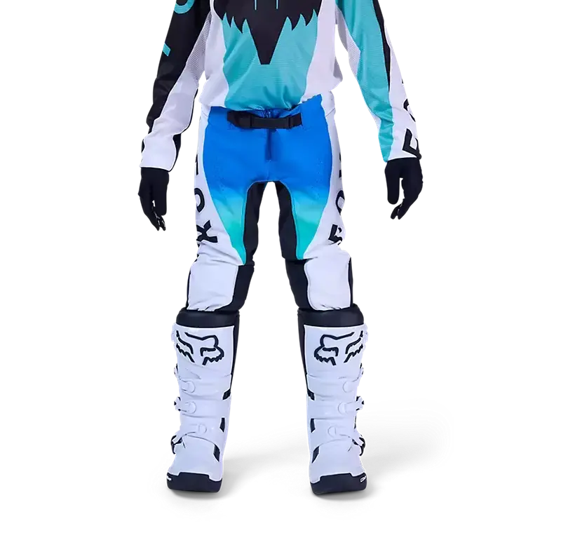Jugendliche Motocross-Fahrerin trägt die blaue Fox Flexair Spire Hose mit Schutzstiefeln auf weißem Hintergrund