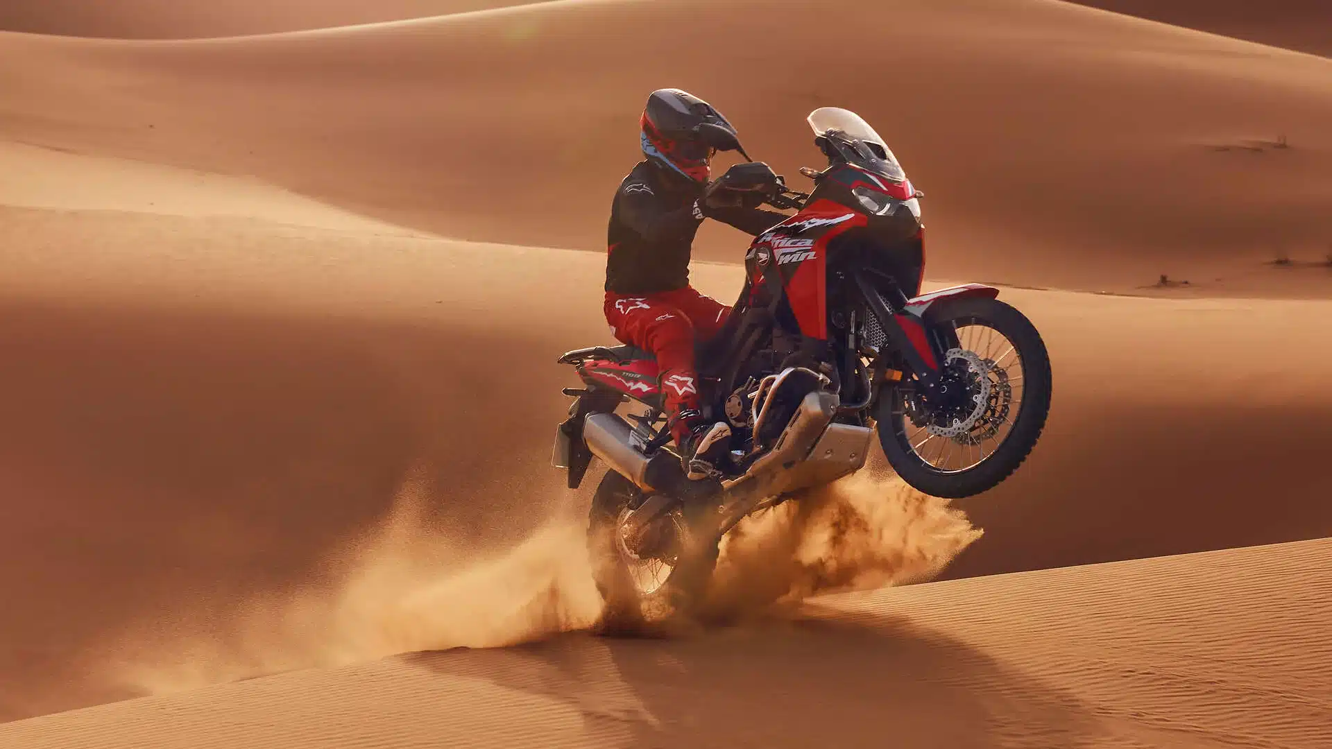 Motorradfahrer auf einer Honda CRF1100L Africa Twin 2024 in einer Sanddüne, hebt das Vorderrad an.