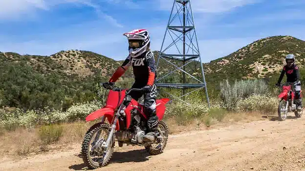 Kinder fahren mit der Honda CRF110F auf einer staubigen Offroad-Piste