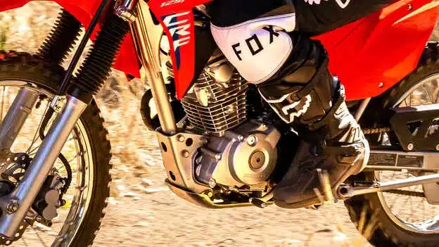 Detailaufnahme des Motors und Fahrwerks einer Honda CRF125F mit Fahrer beim Fahren im Gelände.