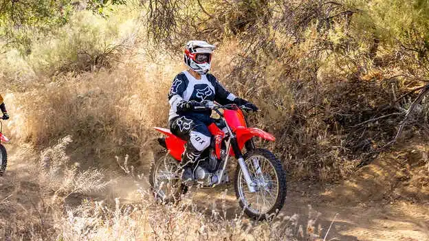 Junger Fahrer fährt auf einer roten Honda CRF125F auf einem staubigen Offroad-Pfad durch trockenes Gelände