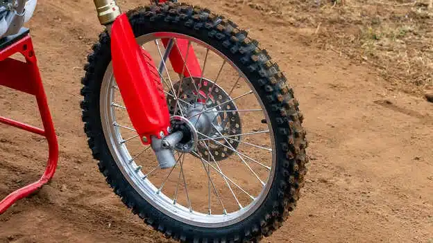 Vorderrad einer Honda CRF150R mit grobstolligem Reifen und roten Gabelschützern auf einer Motocross-Strecke