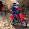 Kinder fahren mit der Honda CRF50F auf einer staubigen Offroad-Strecke.