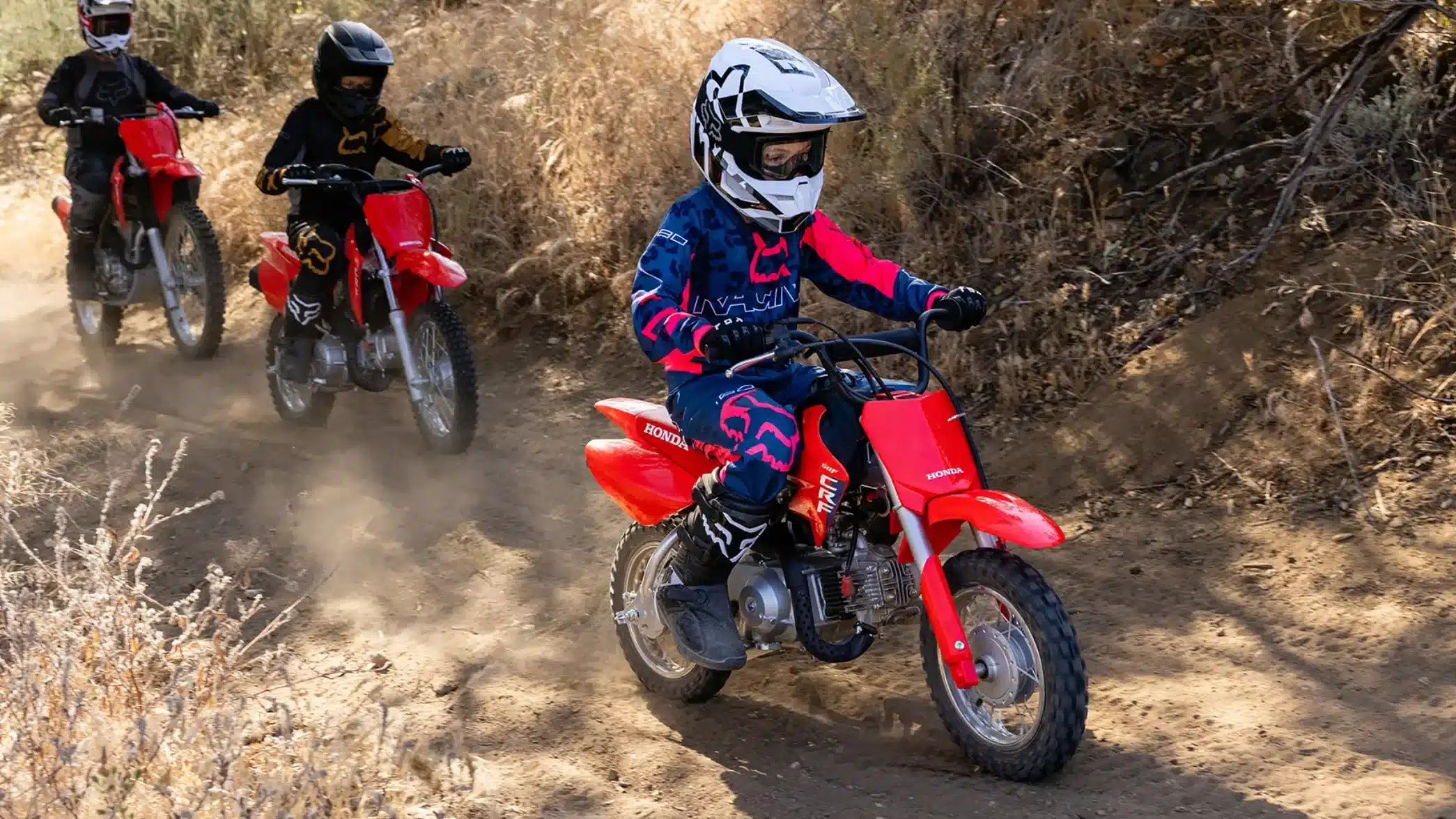 Kinder fahren mit der Honda CRF50F auf einer staubigen Offroad-Strecke.