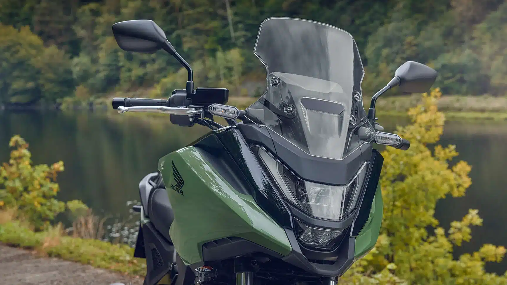 Front der Honda NC750X mit Windschutzscheibe und LED-Scheinwerfer vor einem See.