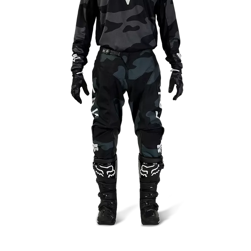 Fox 180 Bnkr Motocross-Hose in Schwarz-Camouflage mit Protektoren und Stiefeln, frontal fotografiert.