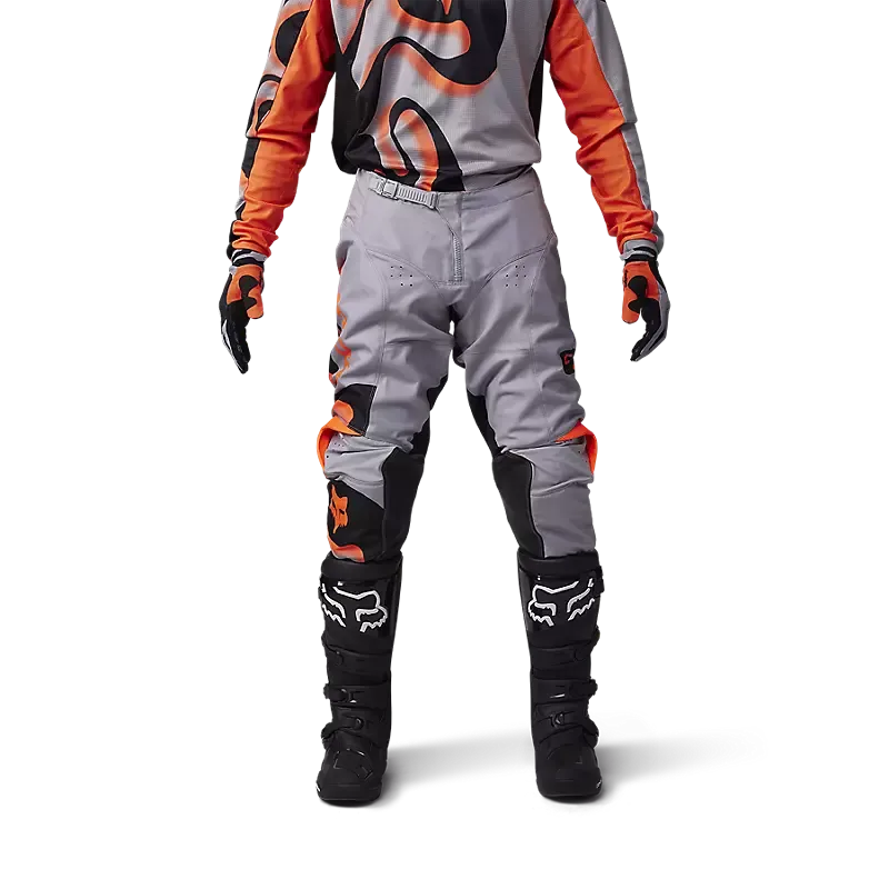 Motocross-Hose Fox 180 Emotion in Grau mit orangen und schwarzen Akzenten, getragen von einer Person mit passendem Oberteil und Stiefeln.