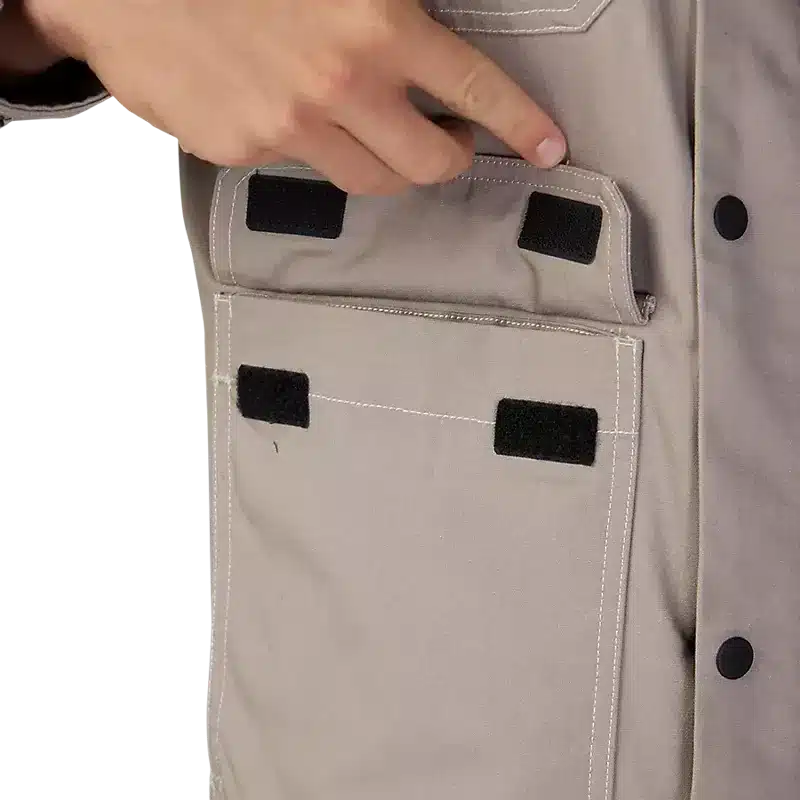 Detailansicht der großen Fronttasche einer taupefarbenen Mercer-Jacke mit Klettverschluss, Hand greift in Tasche