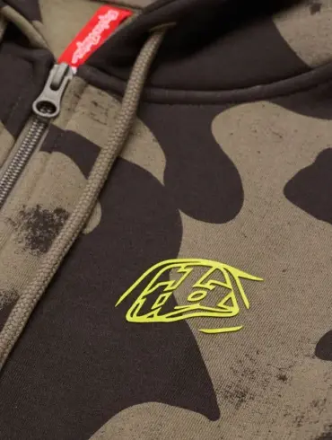 Nahaufnahme eines Kapuzenpullis mit Olivtarn-Muster, Reißverschluss und gelbem Logo.