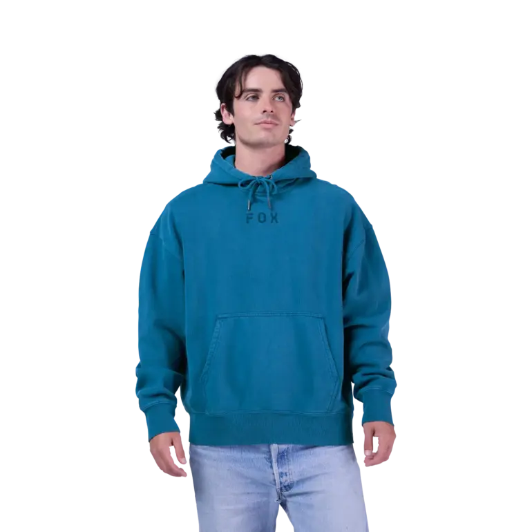 Ein Mann trägt den oversized Wordmark Kapuzenpullover von Fox in Türkis mit Kordelzug und Kängurutasche.