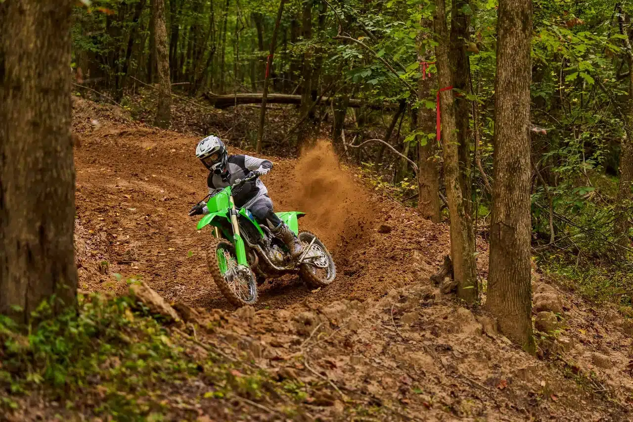 Kawasaki KX450X 2026 Offroad-Motorrad wird von einem Fahrer auf einer schlammigen Strecke durch den Wald gesteuert.