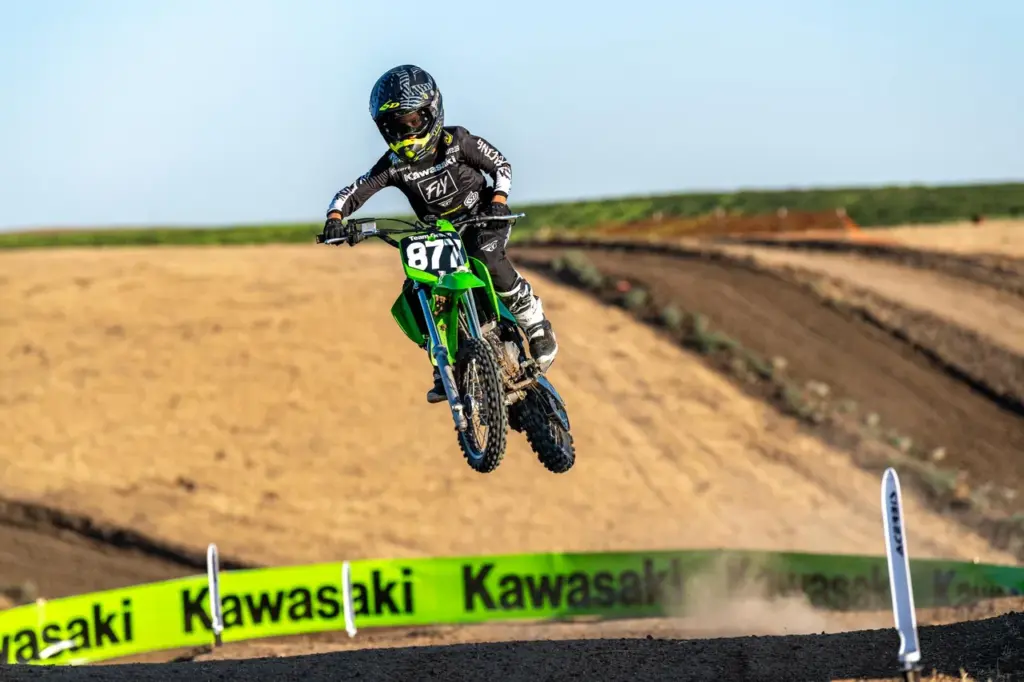 Kind fährt Kawasaki KX65 2026 Motocross-Maschine und springt über eine Geländestrecke