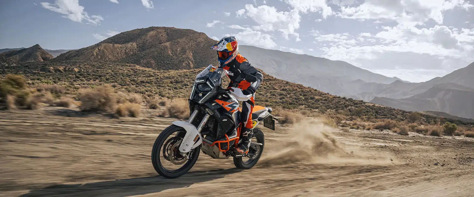 KTM 1390 Super Adventure R fährt im Gelände über eine staubige Piste vor Bergkulisse.