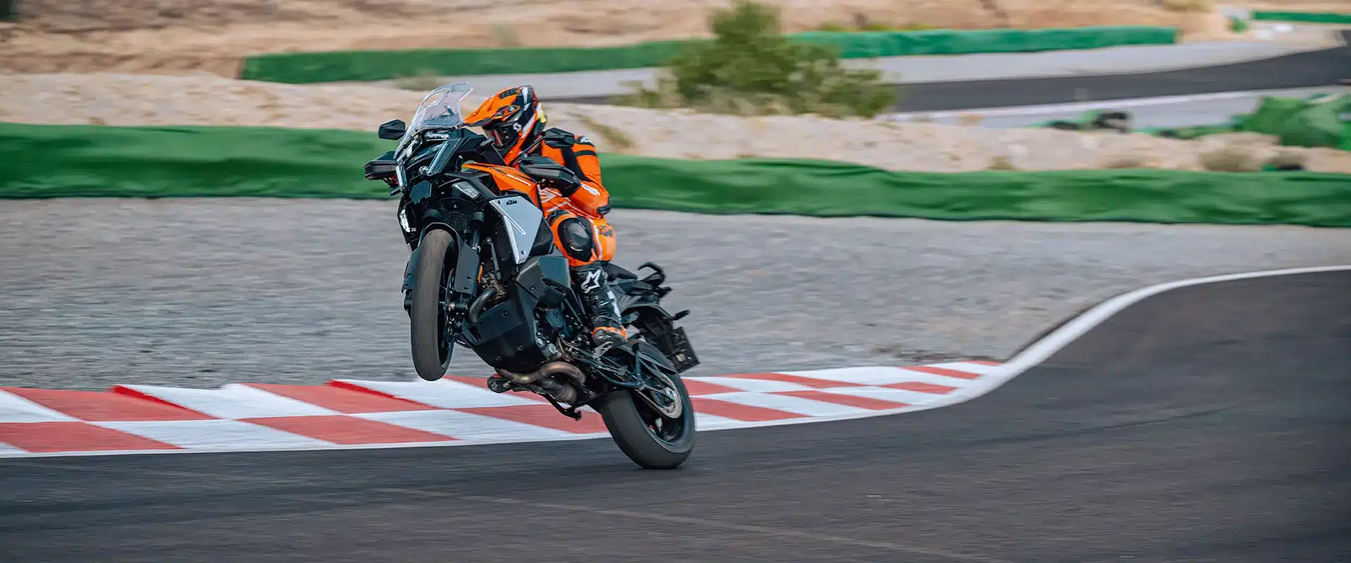 KTM 1390 Super Adventure S EVO fährt auf einer asphaltierten Strecke, Vorderrad in der Luft, Fahrer in orangefarbener Schutzkleidung