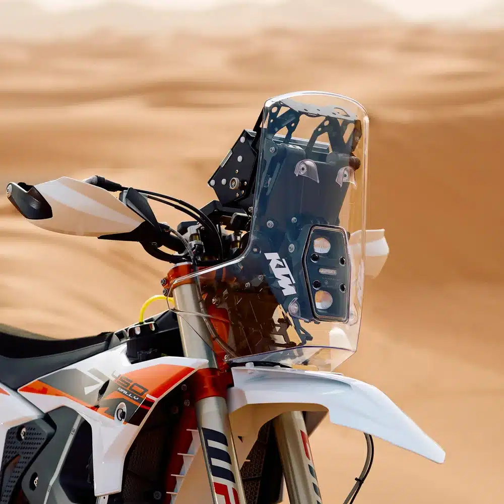 Frontansicht der KTM 450 Rally Replica 2026 mit Navigations-Tower vor Sanddünen