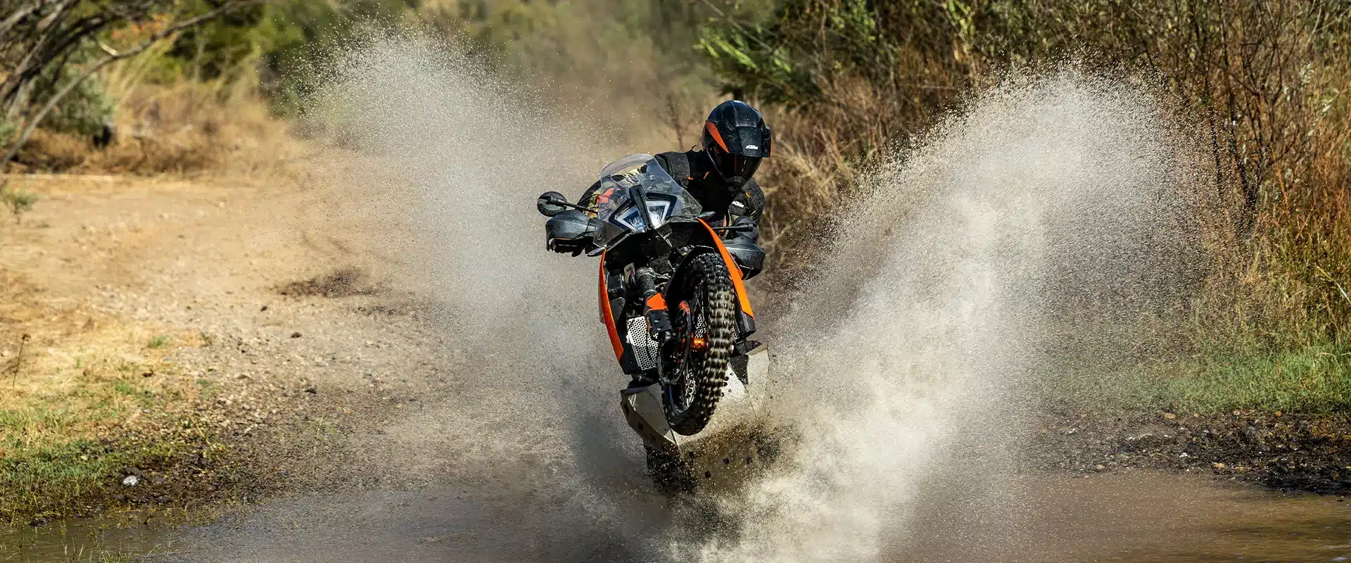 KTM 790 Adventure 2026 hebt im Offroad-Einsatz das Vorderrad beim Durchqueren eines Wasserfeldes an.
