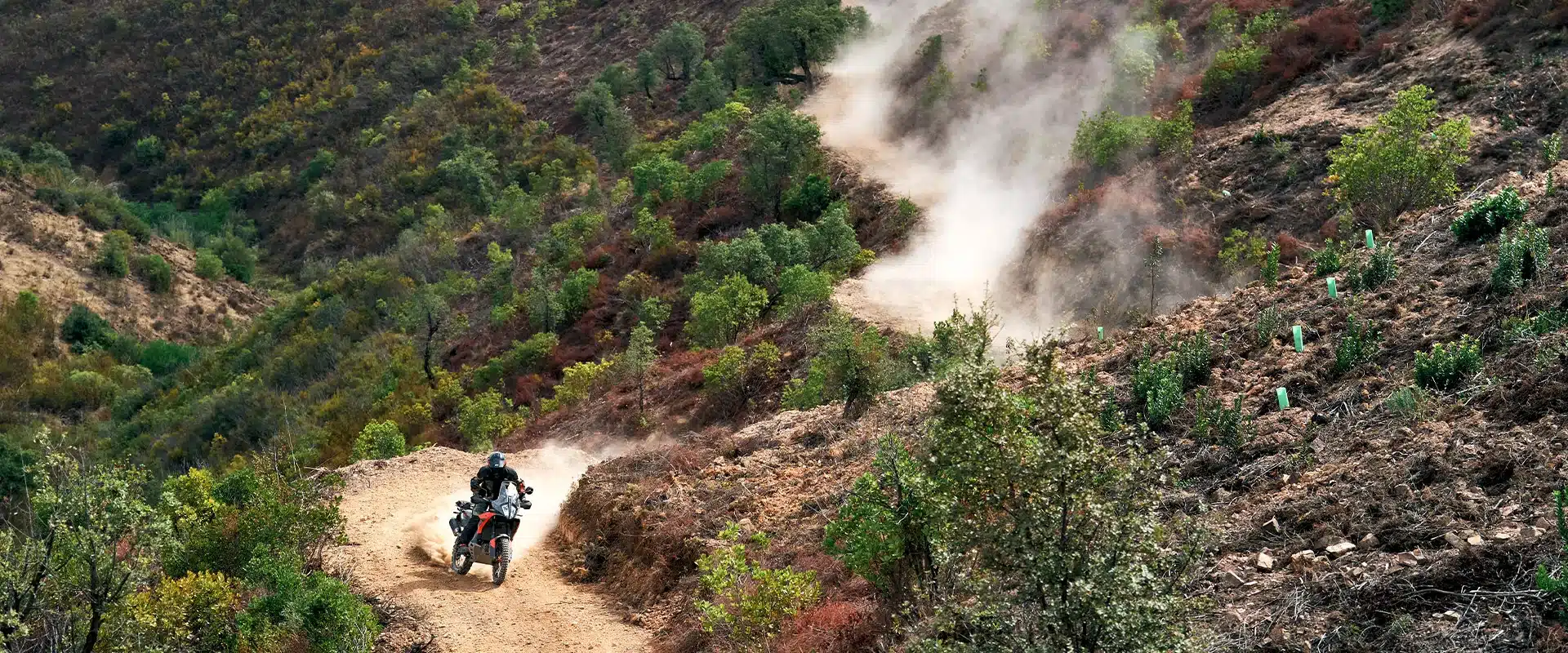 Ein Fahrer steuert die KTM 790 Adventure auf einer staubigen Schotterstraße durch hügeliges Gelände.
