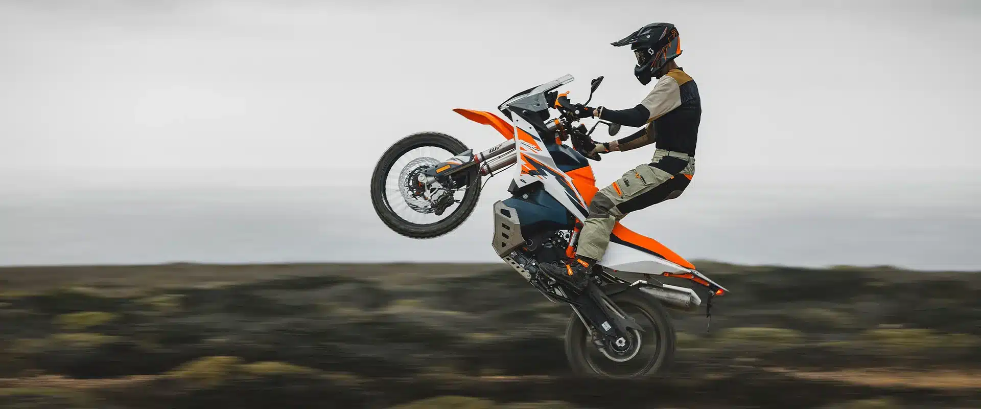 Motorradfahrer auf einer KTM 890 Adventure R 2026 fährt auf dem Hinterrad über eine raue Landschaft.