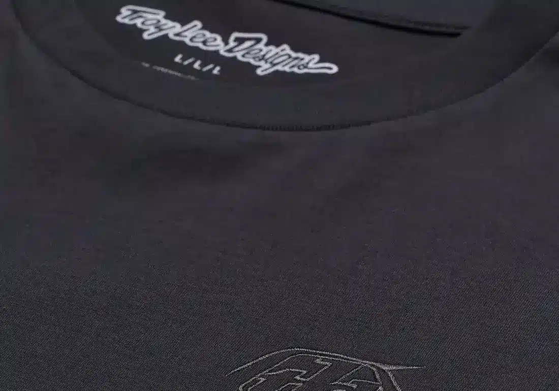 Detailaufnahme eines schwarzen Troy Lee Designs Kurzarm-T-Shirts mit dezentem Logo auf der Brust und Schriftzug im Nackenbereich.