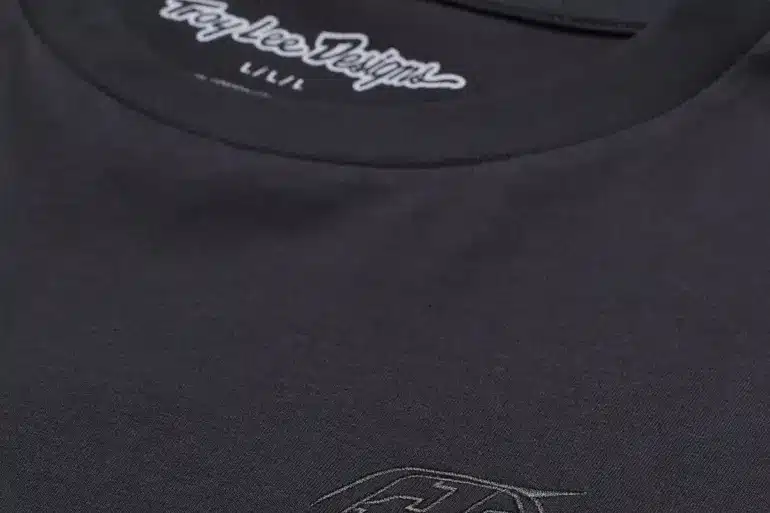 Detailaufnahme eines schwarzen Troy Lee Designs Kurzarm-T-Shirts mit dezentem Logo auf der Brust und Schriftzug im Nackenbereich.