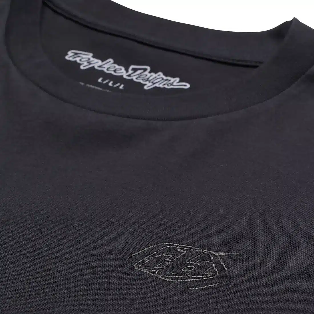 Detailaufnahme eines schwarzen Troy Lee Designs Kurzarm-T-Shirts mit dezentem Logo auf der Brust und Schriftzug im Nackenbereich.