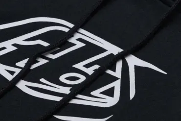 Nahaufnahme eines schwarzen Hoodies mit weißem Badge-Aufdruck und Kapuzenkordeln.