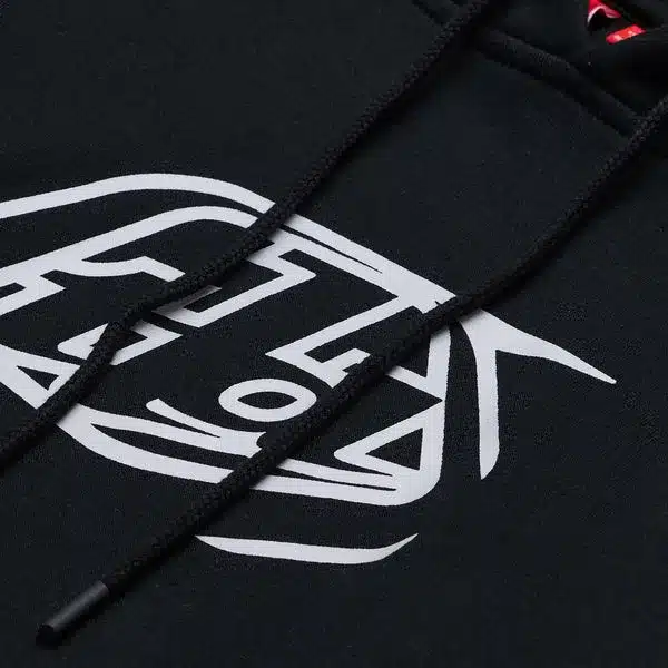 Nahaufnahme eines schwarzen Hoodies mit weißem Badge-Aufdruck und Kapuzenkordeln.