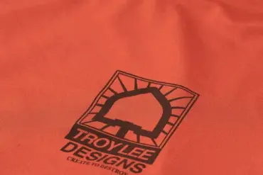 Nahaufnahme des Ruckus Langarm Ride Tee in Ziegelrot mit Troy Lee Designs Logo auf der Brust.