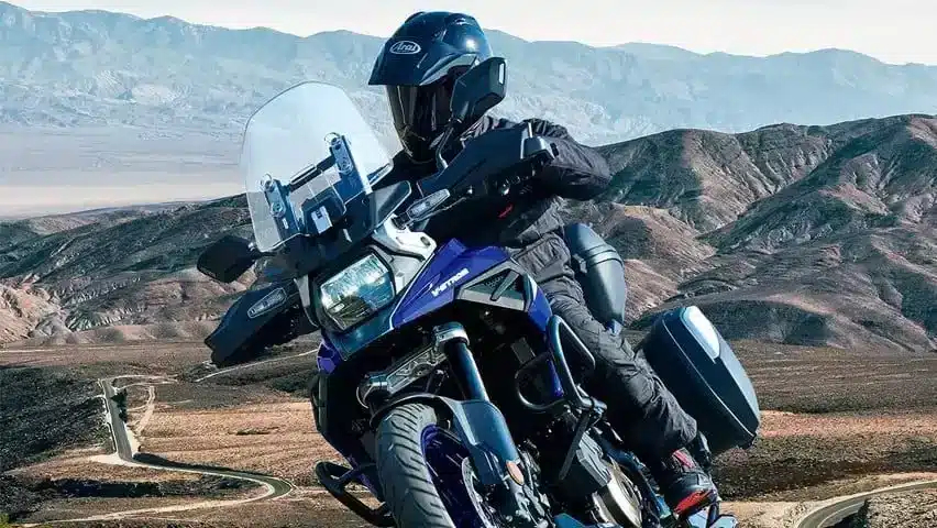 Motorradfahrer auf einer Suzuki V-Strom 1050 Touring Edition mit Seitenkoffern fährt durch eine bergige Wüstenlandschaft.