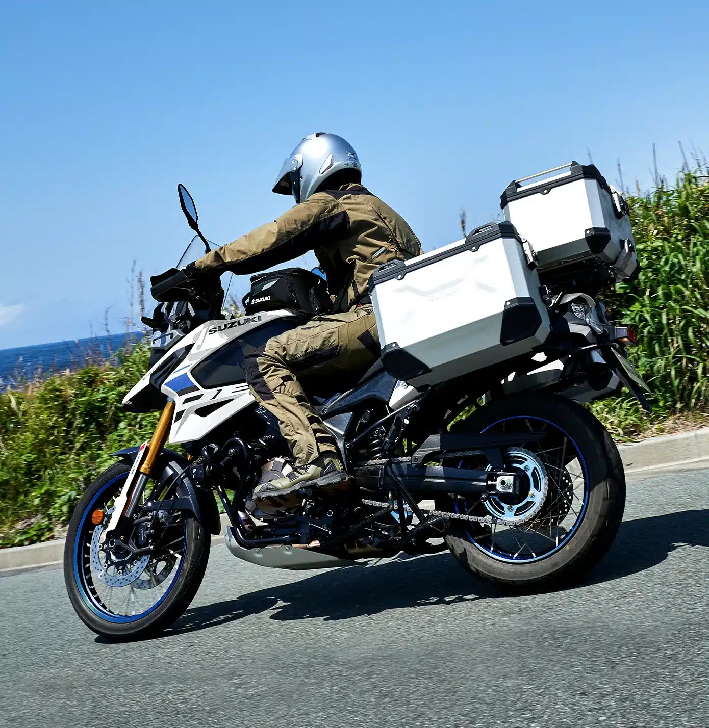 Eine Suzuki V-Strom 1050DE mit Koffern fährt auf einer Landstraße, Fahrer in Adventure-Ausrüstung