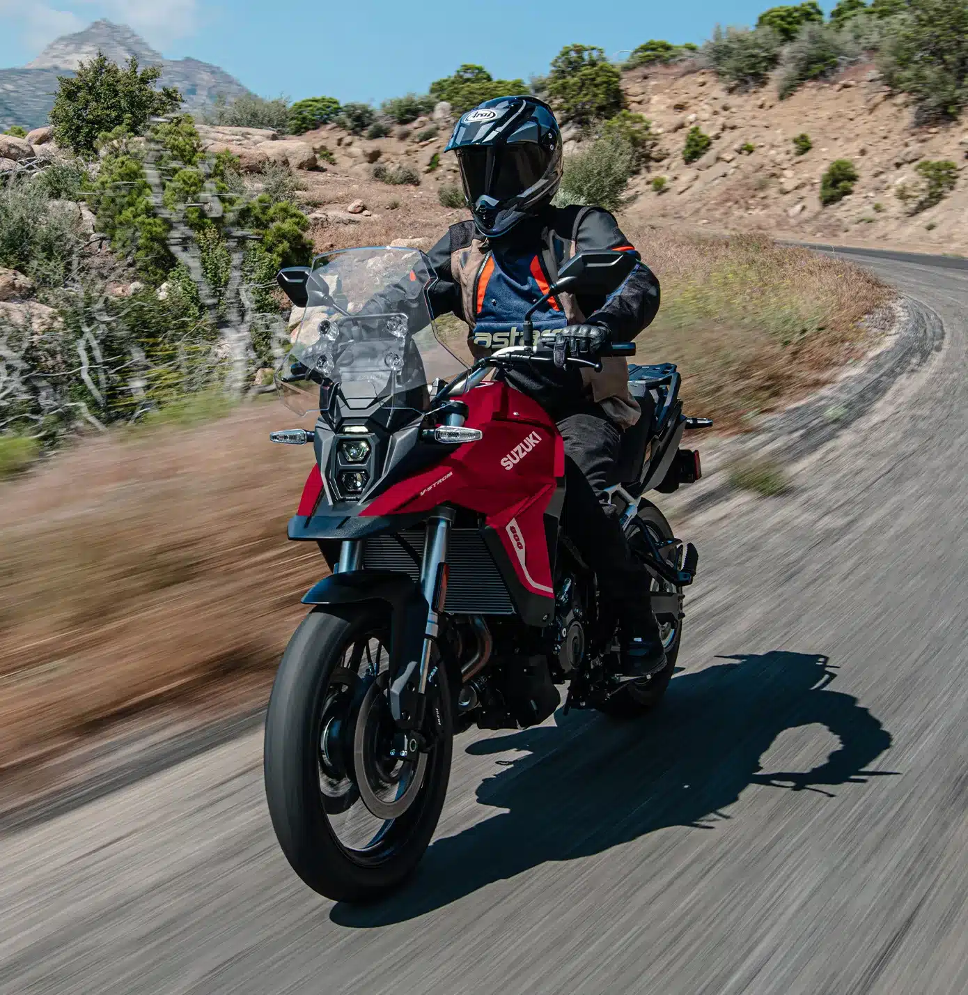 Fahrer auf einer Suzuki V-Strom 800 fährt auf kurviger Landstraße durch bergige Landschaft.