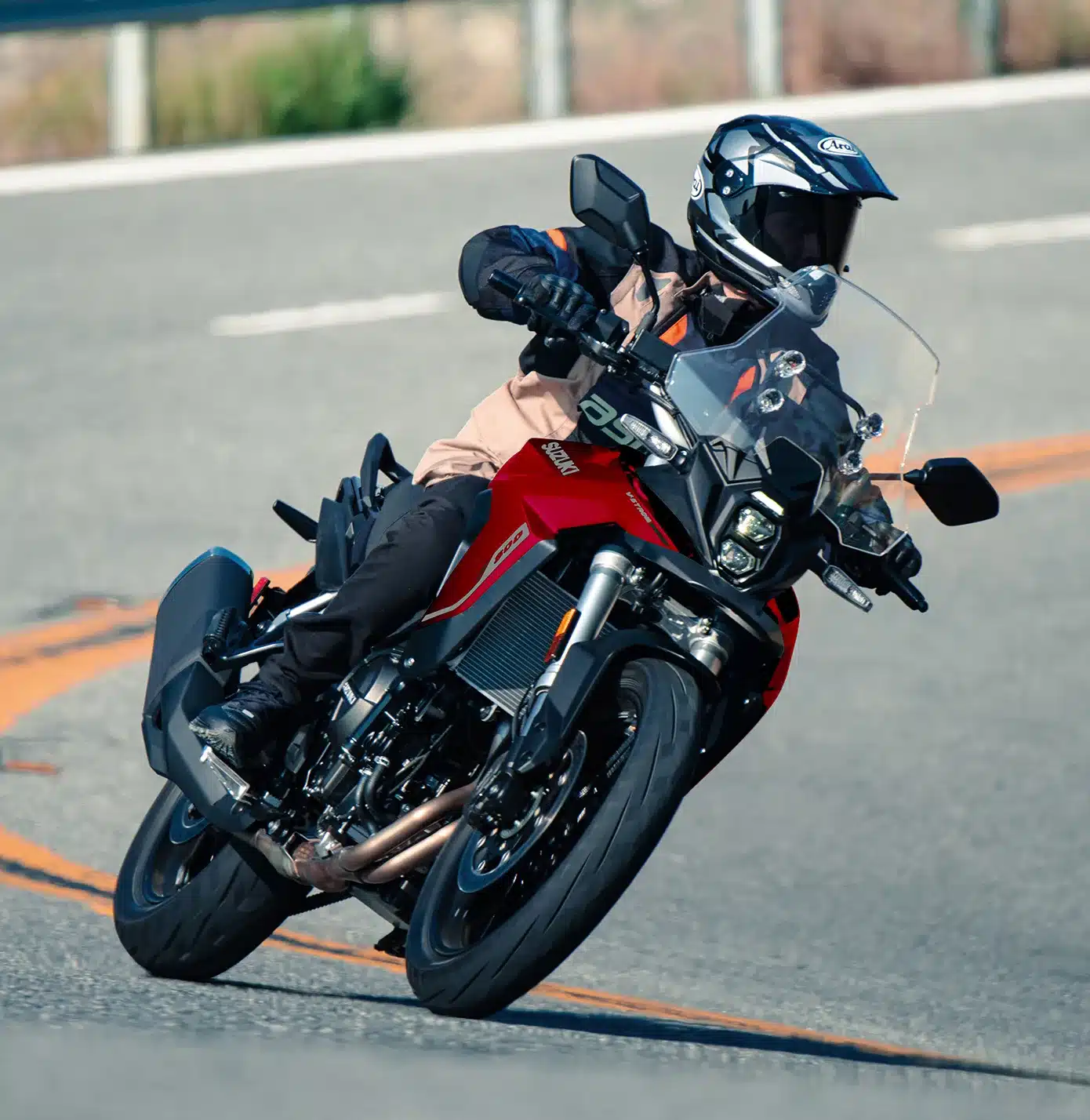 Suzuki V-Strom 800 Motorrad mit Fahrer in voller Schutzkleidung auf einer kurvigen Landstraße.