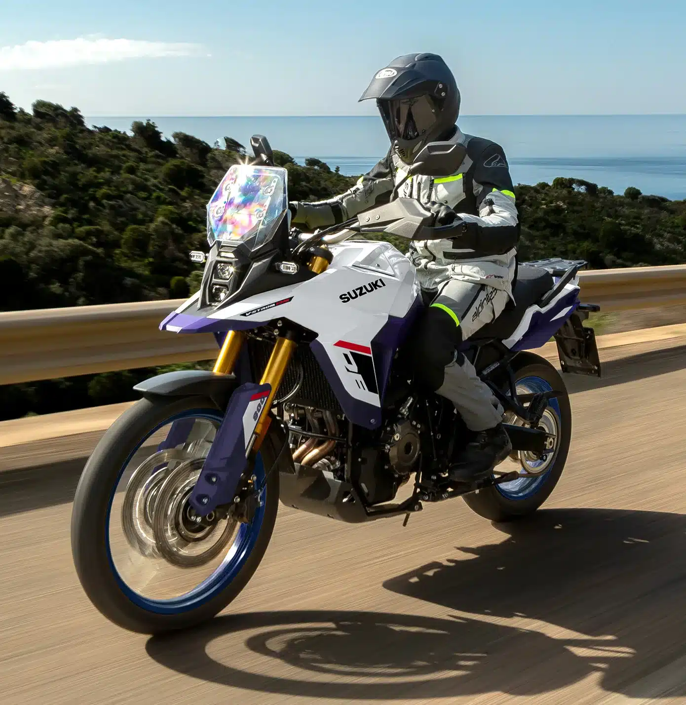 Fahrer auf einer Suzuki V-Strom 800DE fährt auf einer Straße entlang einer Küstenlandschaft.