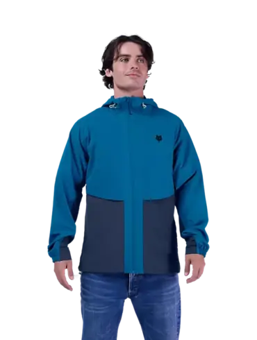Ein Mann trägt die blaue Survivalist Windjacke mit Kapuze und Reißverschluss.