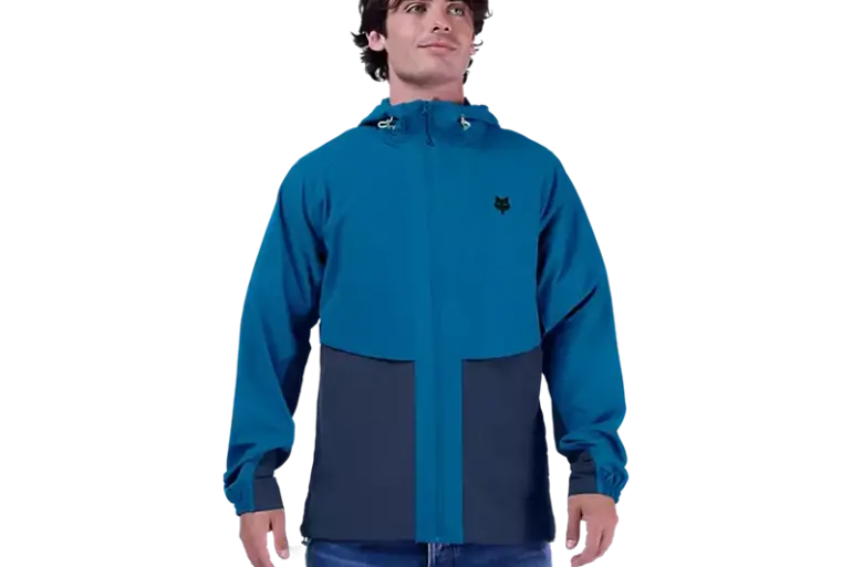 Ein Mann trägt die blaue Survivalist Windjacke mit Kapuze und Reißverschluss.