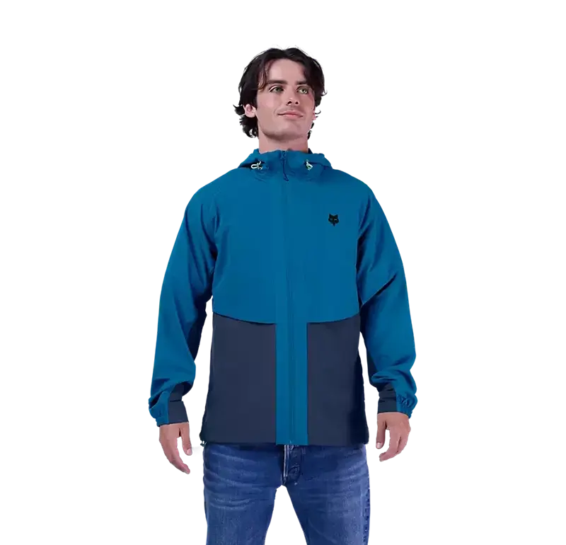 Ein Mann trägt die blaue Survivalist Windjacke mit Kapuze und Reißverschluss.