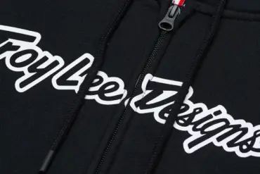 Nahaufnahme des schwarzen Troy Lee Designs Zip Up Hoodie Signature mit Reißverschluss und weißem Logo-Schriftzug.