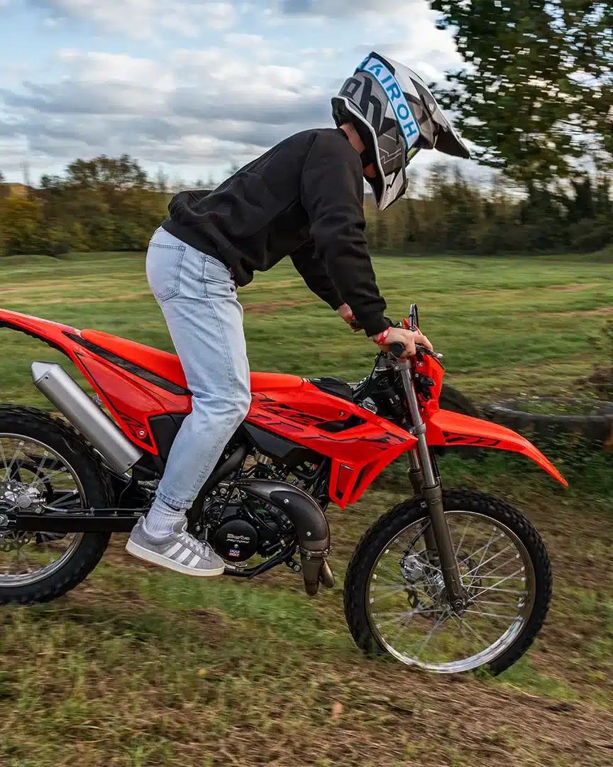 Beta RR 2T 50 Enduro 2025 in Aktion auf einer Wiese, junger Fahrer mit Helm, Motorrad in rotem Design.