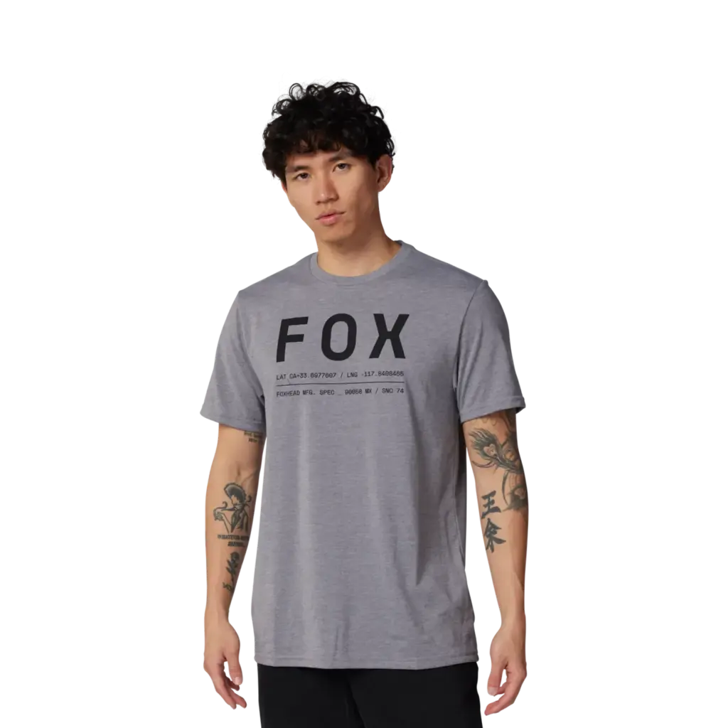 Mann trägt ein graues FOX Non Stop Funktions-T-Shirt mit schwarzem Logoaufdruck, stehend vor neutralem Hintergrund