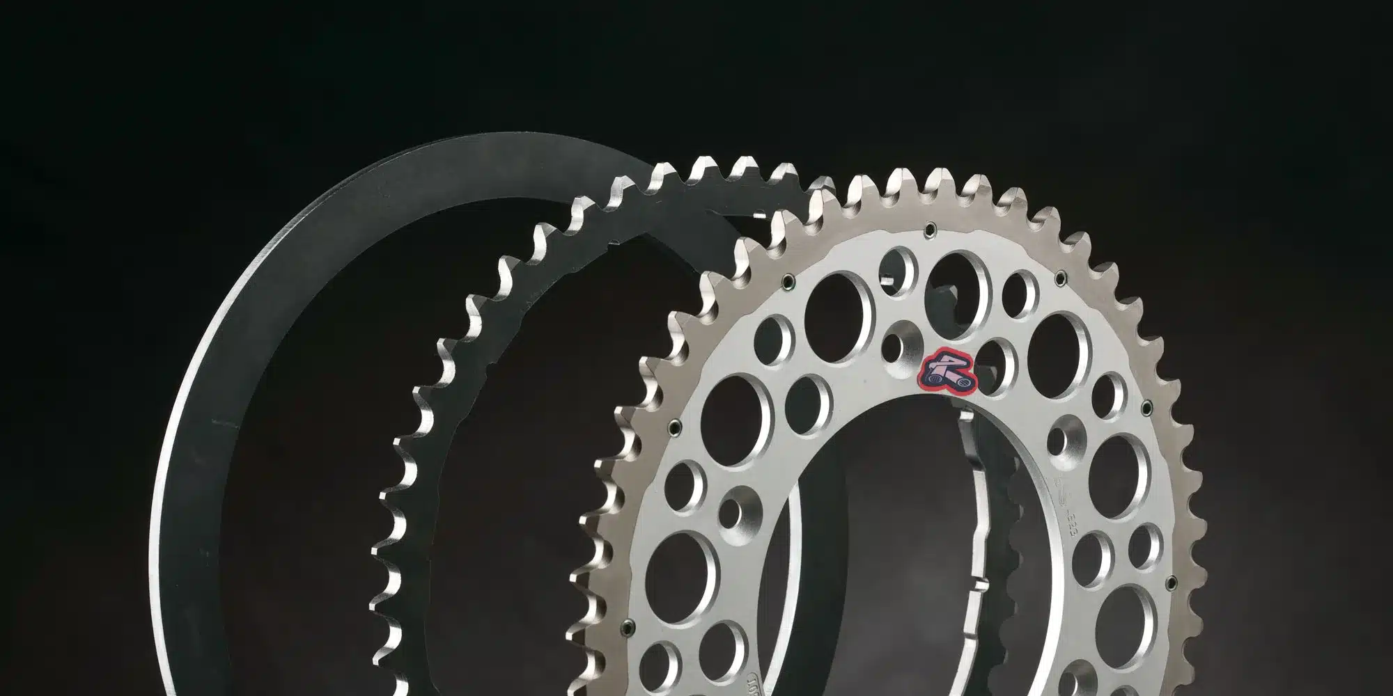 Explosionsdarstellung des Renthal Twinring Kettenrads mit Aluminiumkern und Stahlaußenring vor schwarzem Hintergrund