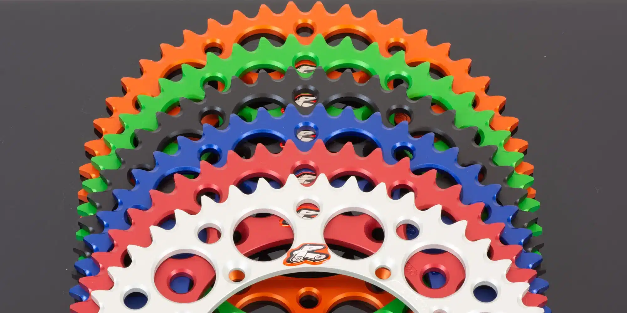 Mehrfarbige CNC-gefräste Renthal Kettenräder aus Aluminium, gestapelt vor schwarzem Hintergrund.