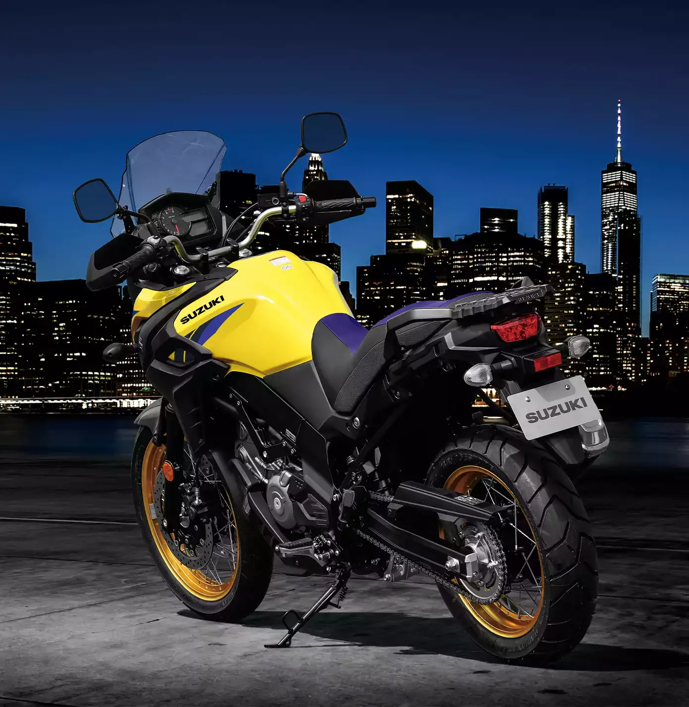 Suzuki V-Strom 650XT Touring Edition, gelbe Ausführung, vor nächtlicher Skyline, seitliche Rückansicht.