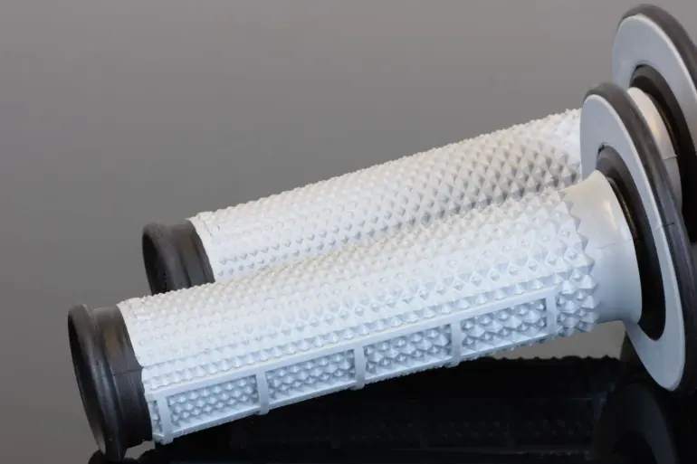 Weiße Tapered MX Griffe mit markanter Diamantstruktur und breitem Flansch auf spiegelndem Untergrund
